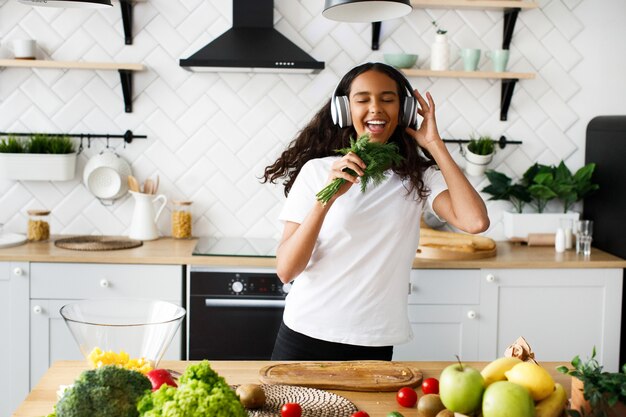 Young african woman is jovially listening to music via headphones and holds dill