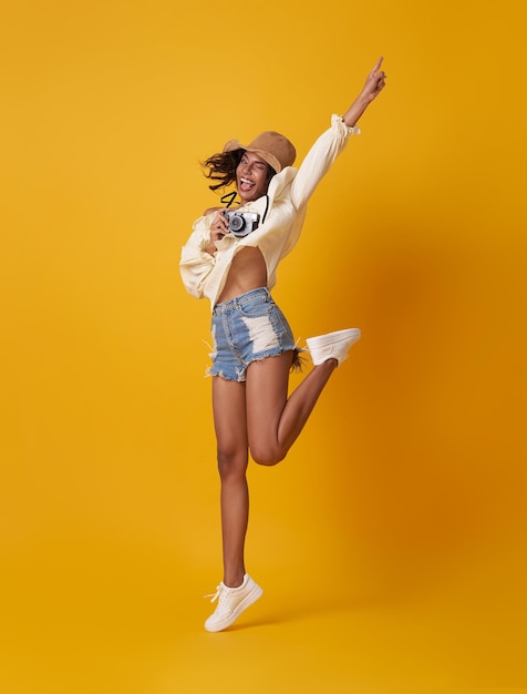 Young african woman tourist smiling and jumping with camera in hand isolated on yellow background