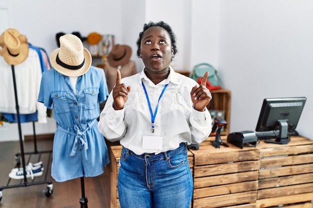 Free photo young african woman working as manager at retail boutique amazed and surprised looking up and pointing with fingers and raised arms.