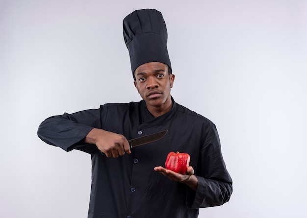 Free photo young afro-american cook in chef uniform holds knife and tomato isolated on white background with copy space