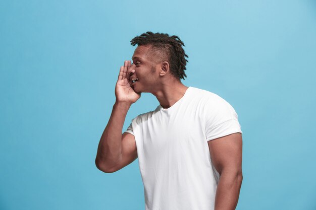 The young afro-american man whispering a secret behind her hand over blue background