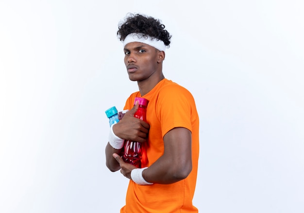 young afro-american sporty man wearing headband and wristband holding water bottle 