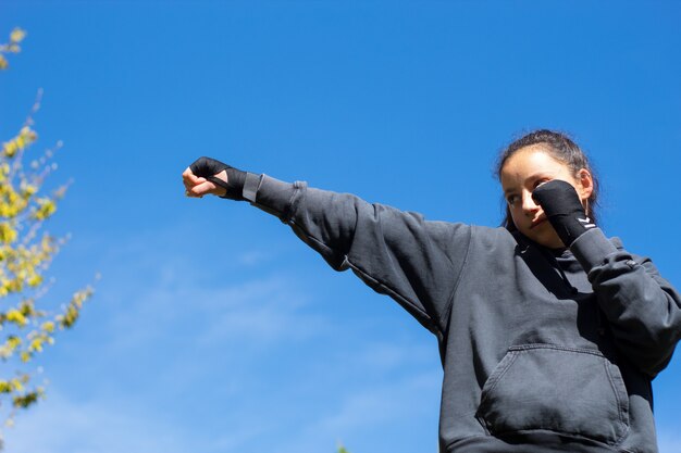 武道を訓練し、海と青い空を背景に屋外でボクシングをする若いアフロ黒人の女の子。態度、スポーツ、トレーニング。コピースペース Premium写真