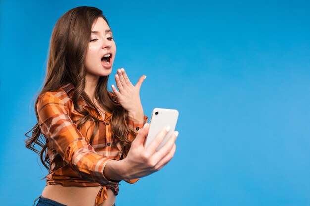 사진을 찍고 있는 매혹적인 소녀 그녀는 스마트폰으로 서서 셀카를 찍고 있다