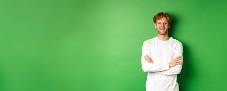 Free Photo young ambitious man with red hair standing over green background holding hands crossed on chest and
