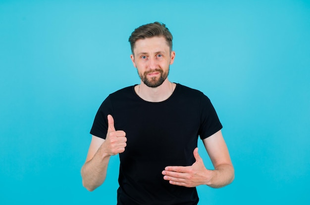 Free photo young amn is showing perfect gesture with thumb on blue background