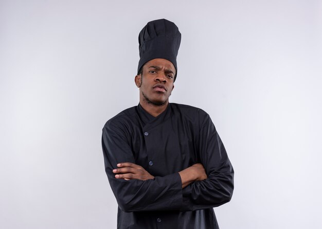 Young annoyed afro-american cook in chef uniform crosses arms and looks at camera isolated on white background with copy space