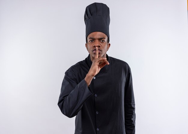 Young annoyed afro-american cook in chef uniform gestures silence hand sign isolated on white background with copy space