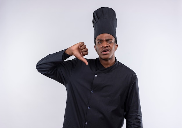Молодой раздраженный афро-американский повар в униформе шеф-повара показывает палец вниз и смотрит в камеру, изолированную на белом фоне с копией пространства