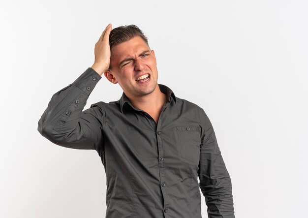 Young annoyed blonde handsome man holds head looking at camera isolated on white background with copy space