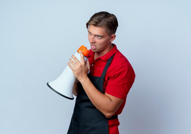 Young annoyed blonde male barber in uniform holds loud speaker rolling eyes isolated on white background with copy space
