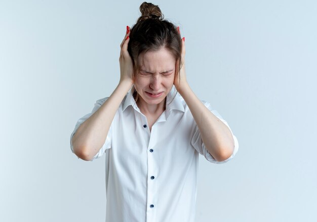 Young annoyed blonde russian girl closses ears with hands isolated on white space with copy space