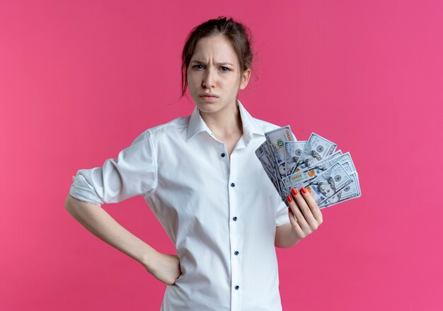 Free photo young annoyed blonde russian girl holds money looking at camera on pink with copy space