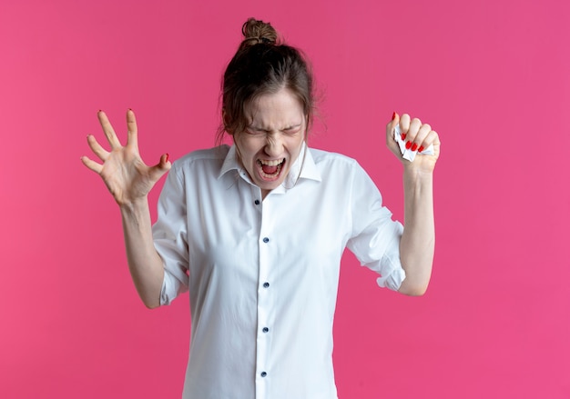 Foto gratuita la giovane ragazza russa bionda infastidita preme la carta in mano e stringe un'altra mano isolata sullo spazio rosa con lo spazio della copia