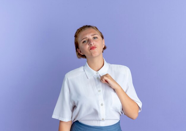 Young annoyed blonde russian girl stands with raised fist isolated on purple background with copy space