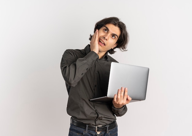 Young annoyed handsome caucasian man holds laptop and looks up isolated on white background with copy space