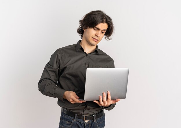 Young annoyed handsome caucasian man holds and looks at laptop isolated on white background with copy space