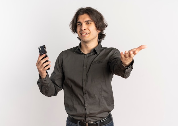 Young annoyed handsome caucasian man holds phone and points at camera isolated on white background with copy space