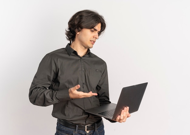 Young annoyed handsome caucasian man looks and points at laptop isolated on white background with copy space