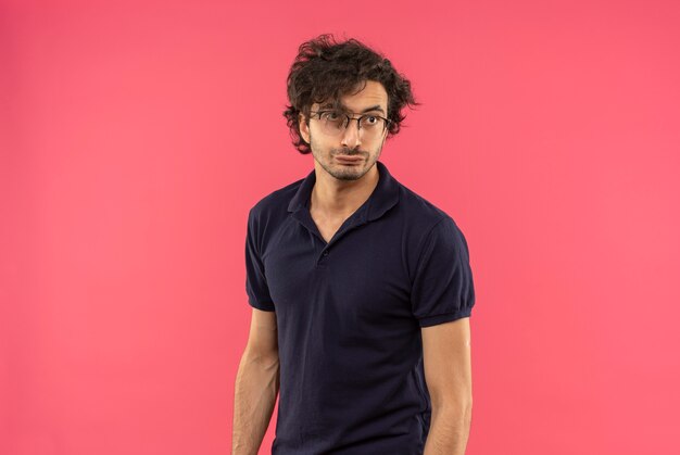 Free photo young annoyed man in black shirt with optical glasses looks at side isolated on pink wall