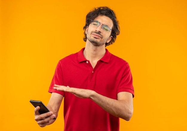 광학 안경 빨간 셔츠에 젊은 화가 남자 보유하고 오렌지 벽에 고립 된 닫힌 눈으로 전화에서 포인트