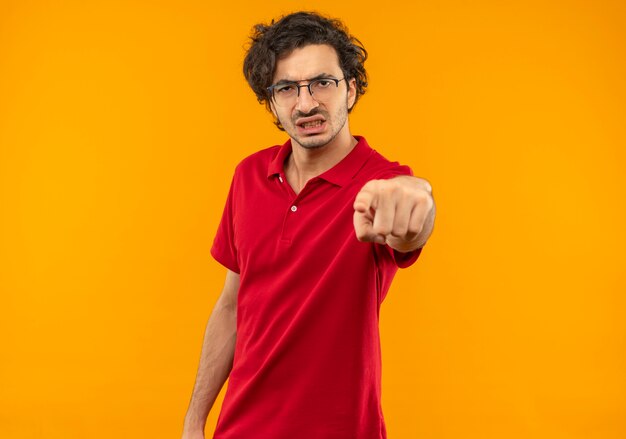 오렌지 벽에 고립 된 광학 안경 포인트와 빨간 셔츠에 젊은 화가 남자