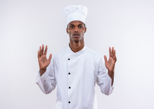 シェフの制服を着た若い気になるアフリカ系アメリカ人の料理人は、コピースペースと白い背景で隔離の手を持ち上げます