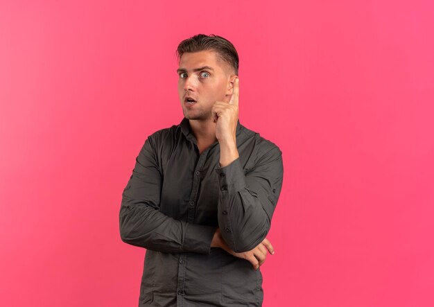 Young anxious blonde handsome man points up isolated on pink background with copy space