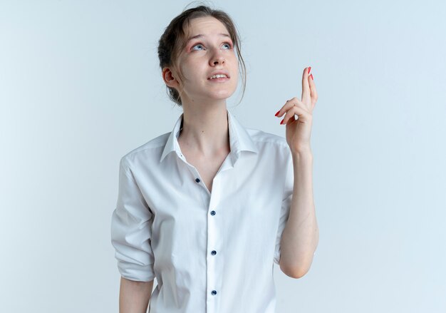 Young anxious blonde russian girl crosses fingers looking up isolated on white space with copy space