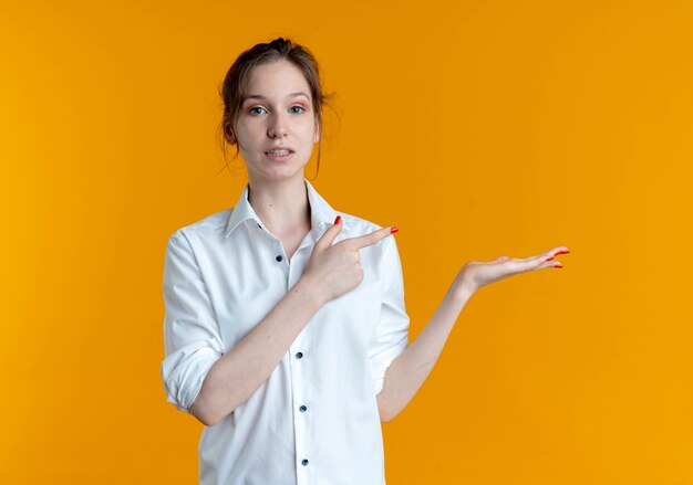 복사 공간 오렌지 배경에 고립 된 빈 손으로 젊은 불안 금발 러시아 여자 포인트