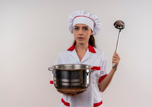 Молодая взволнованная кавказская девушка-повар в униформе шеф-повара держит горшок и ковш, изолированные на белом фоне с копией пространства