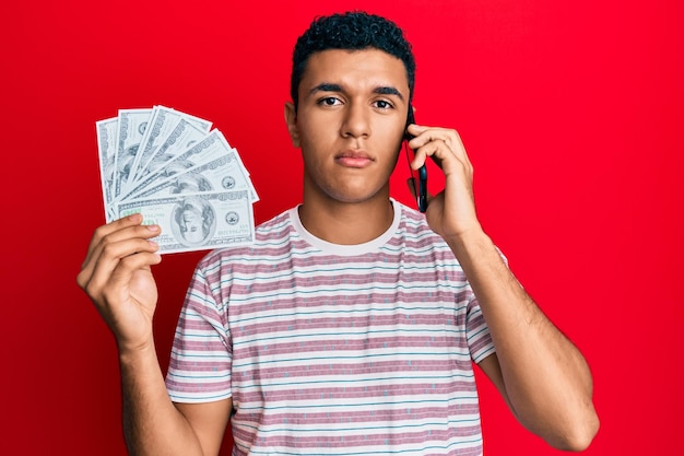 Free photo young arab man having conversation talking on the smartphone holding dollars relaxed with serious expression on face simple and natural looking at the camera