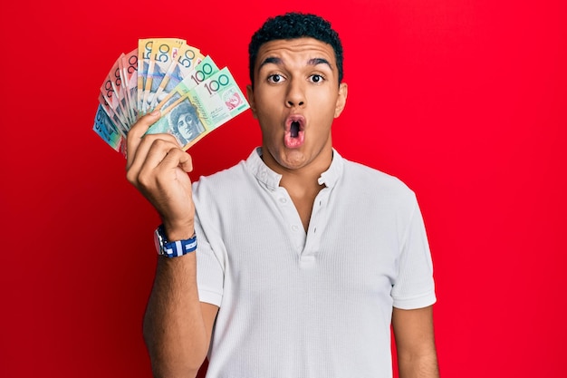 Free photo young arab man holding australian dollars scared and amazed with open mouth for surprise disbelief face