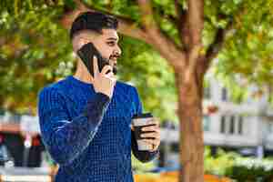 Free photo young arab man talking on the smartphone drinking coffee at park