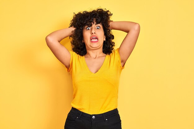 孤立した黄色の背景の上に立って T シャツを着た巻き毛の若いアラブ女性