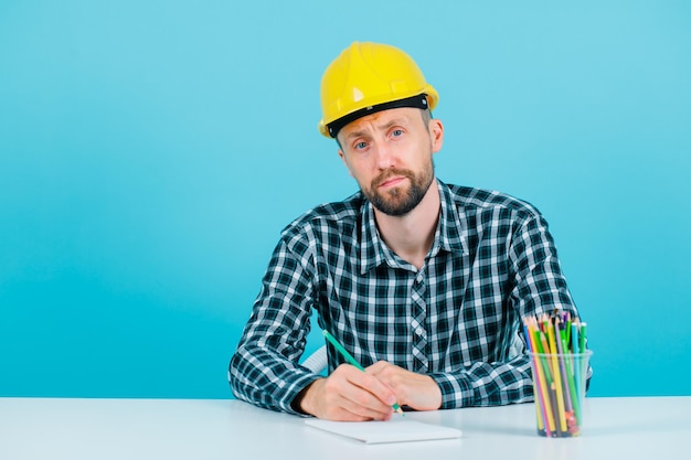 Free photo young architect is looking at camera by sitting on blue background