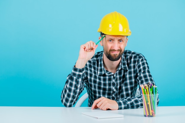 Free photo young architect is thinking by holding pencil on temple on blue background