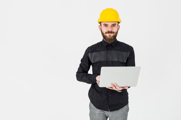 Young architect wearing yellow hardhat holding portable laptop