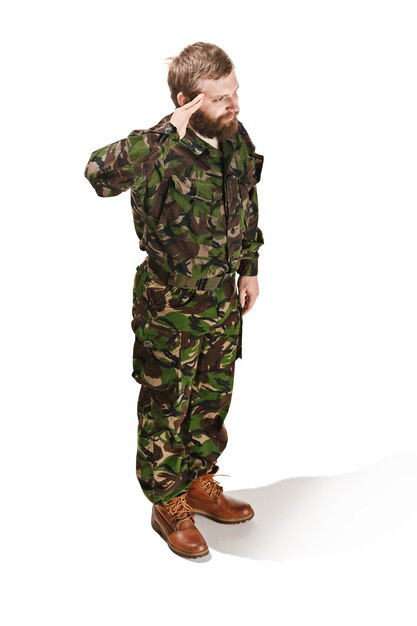 Young army soldier wearing camouflage uniform standing and saluting isolated on white studio background in full-length. Young caucasian model. Military, soldier, army concept. Proffeshional concepts