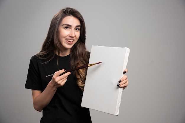 Young artist in black shirt posing with brush and canvas. 