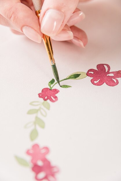 직장에서 종이에 수채화 물감 페인트와 브러시로 꽃 패턴을 그리는 젊은 예술가