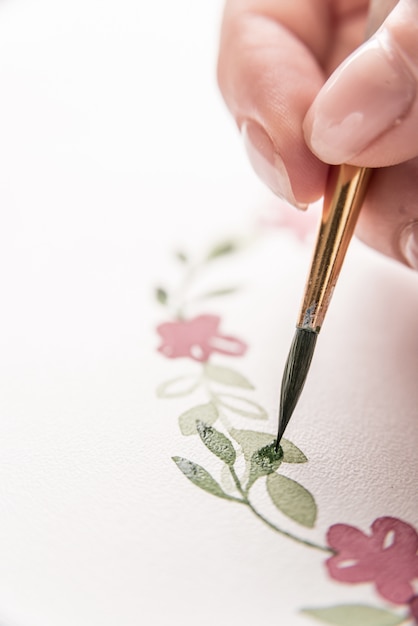 Young artist drawing flowers pattern with watercolor paint and brush on paper at workplace