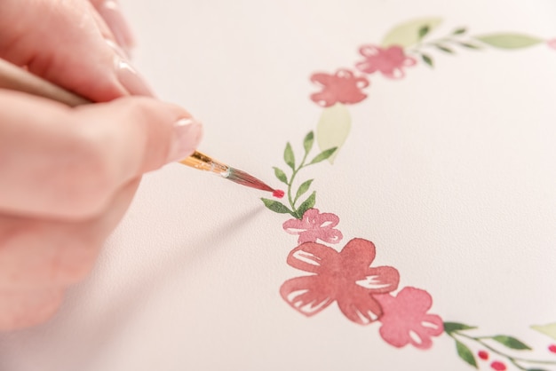 水彩絵の具とブラシで職場で紙の上に花のパターンを描く若いアーティスト