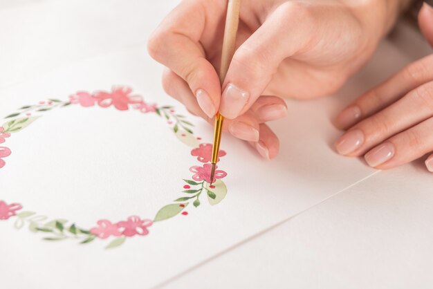 Young artist drawing flowers pattern with watercolor paint and brush on paper at workplace