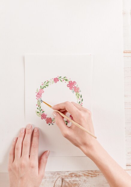직장에서 종이에 수채화 물감 페인트와 브러시로 꽃 패턴을 그리는 젊은 예술가