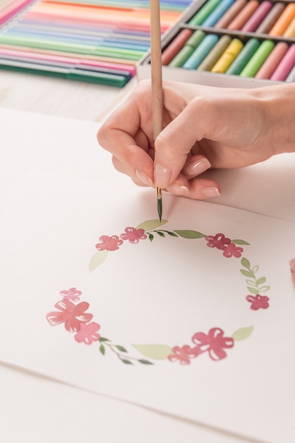 若いアーティストが水彩絵の具や職場でブラシで花のパターンを描画