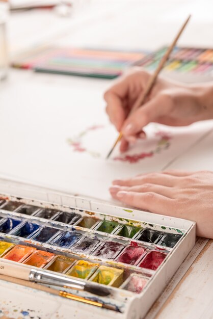 Молодой художник рисует цветочный узор акварельной краской и кистью на рабочем месте