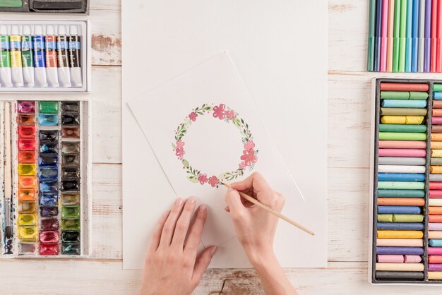 Young artist drawing flowers pattern with watercolor paint and brush at workplace