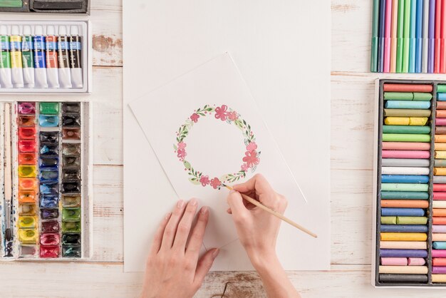 若いアーティストが水彩絵の具や職場でブラシで花のパターンを描画