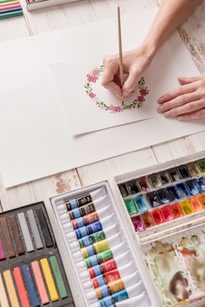 Young artist drawing flowers pattern with watercolor paint and brush at workplace